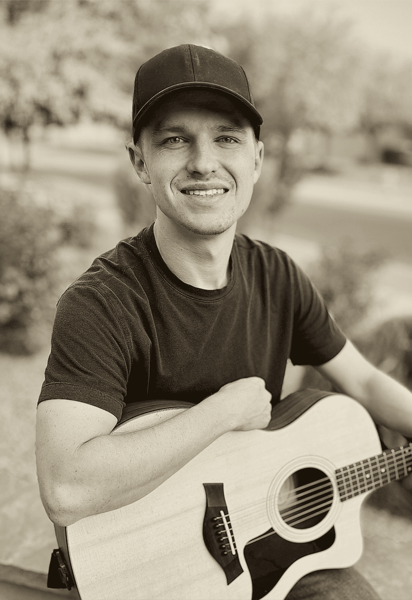 Tyler Downey smiling outdoors with his acoustic guitar